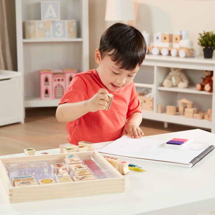 A kid playing with the Melissa & Doug Stamp-a-Scene Stamp Pad: Fairy Garden - 20 Wooden Stamps, 5 Colored Pencils, and 2-Color Stamp Pad