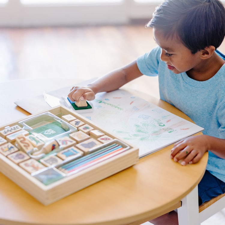 A kid playing with the Melissa & Doug Stamp-a-Scene Stamp Set: Rain Forest - 20 Wooden Stamps, 5 Colored Pencils, and 2-Color Stamp Pad