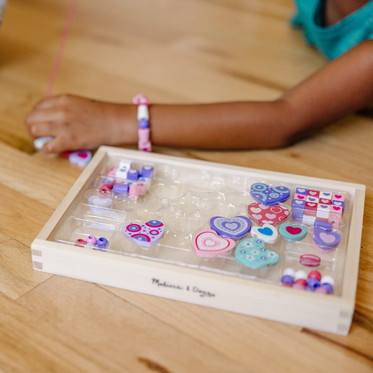 A kid playing with the Melissa & Doug Created by Me! Heart Beads Wooden Bead Kit, 120+ Beads and 5 Cords for Jewelry-Making