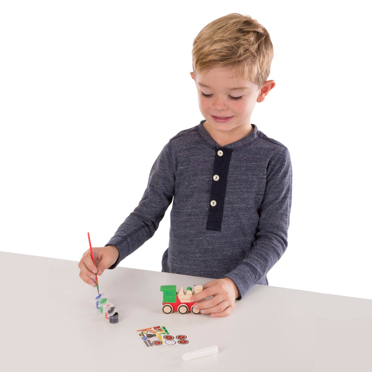 A child on white background with the Melissa & Doug Train Wooden Craft Kit