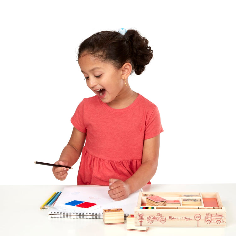 A child on white background with the Melissa & Doug Wooden Stamp Set: Vehicles - 10 Stamps, 5 Colored Pencils, 2-Color Stamp Pad