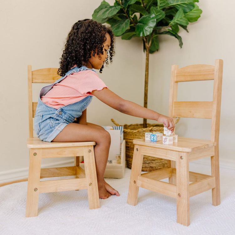 A kid playing with the Melissa & Doug Solid Wood Chairs, Set of 2 - Light Finish Furniture for Playroom