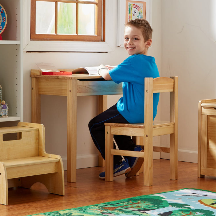 A kid playing with the Melissa & Doug Wooden Child's Lift-Top Desk & Chair - Honey