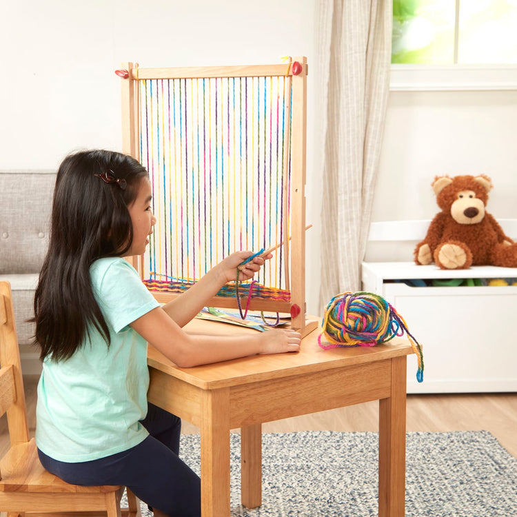 A kid playing with the Melissa & Doug Wooden Multi-Craft Weaving Loom: Extra-Large Frame (22.75 x 16.5 inches)