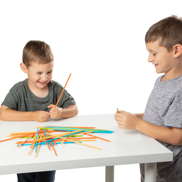 A child on white background with the Melissa & Doug Wooden Pick-Up Sticks Tabletop Game with 41 Colorful Wooden Pieces in Wooden Storage Box