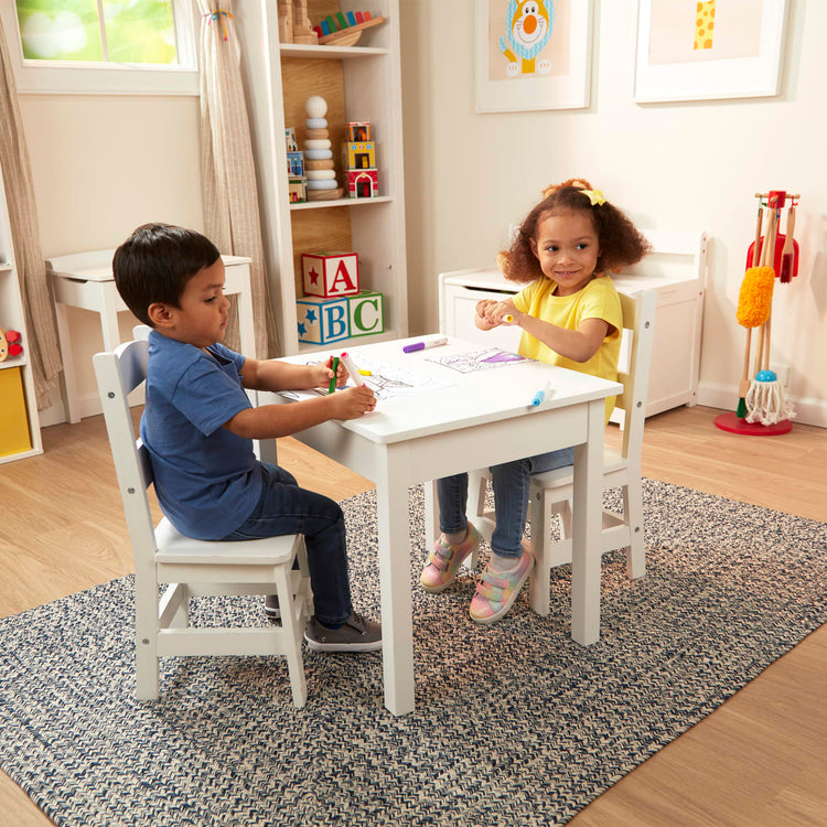 A kid playing with the Melissa & Doug Wooden Kids Table and 2 Chairs Set - White Furniture for Playroom