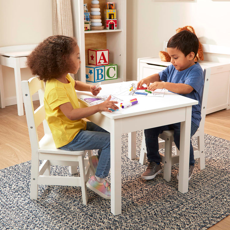 A kid playing with the Melissa & Doug Wooden Kids Table and 2 Chairs Set - White Furniture for Playroom