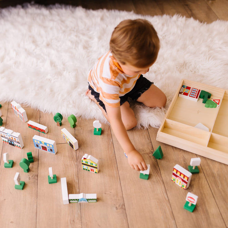 A kid playing with the Melissa & Doug Wooden Town Play Set With Storage Tray (32 pcs)