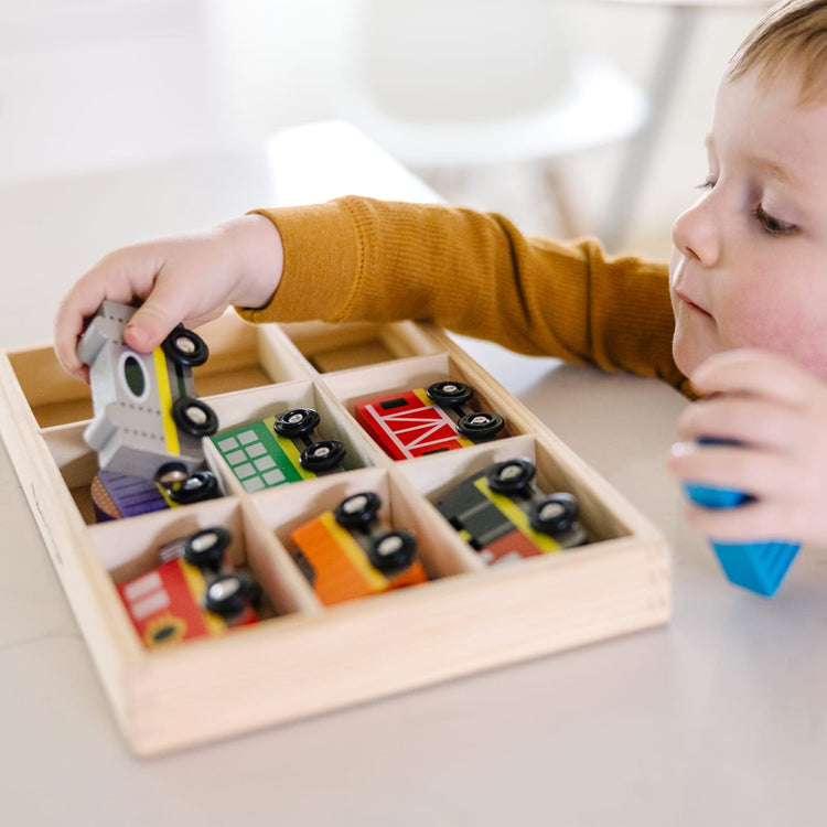 A kid playing with the Melissa & Doug Wooden Train Cars - 8 3-Inch Wheeled Trains in Crate